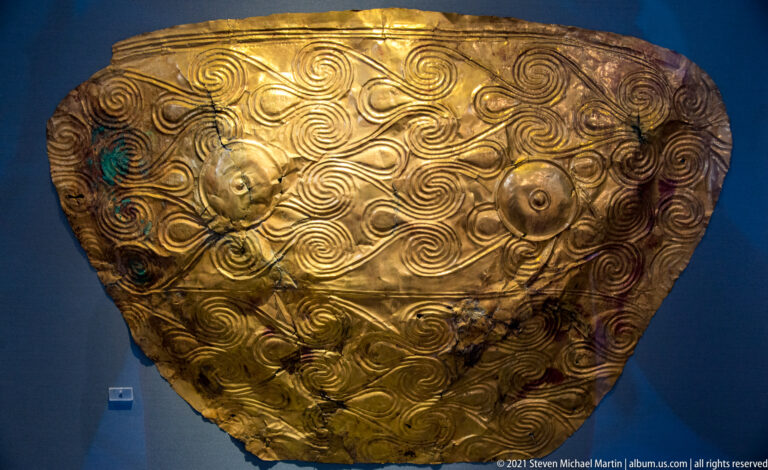Large curved gold sheet with dense repoussé spirals and two raised circular bosses resembling a funerary chest covering.