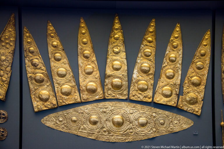 Group of long pointed gold plaques with embossed circular motifs and an oval gold ornament beneath them.