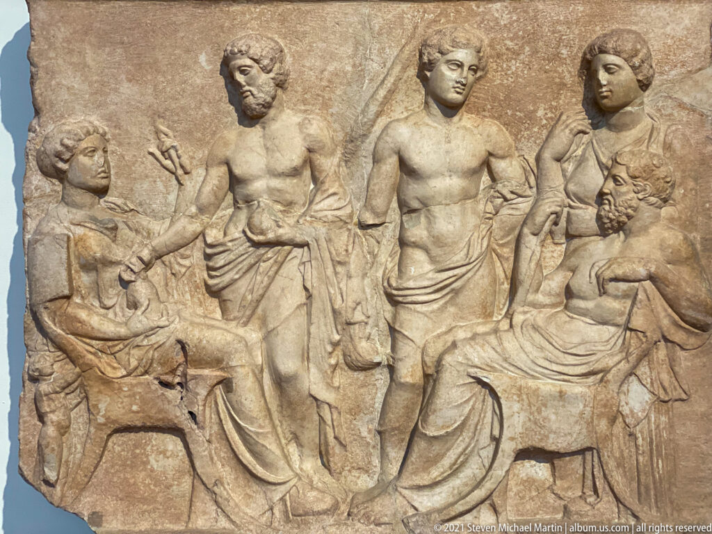 Marble relief with seated and standing adults and smaller attendants arranged in a domestic or commemorative scene.