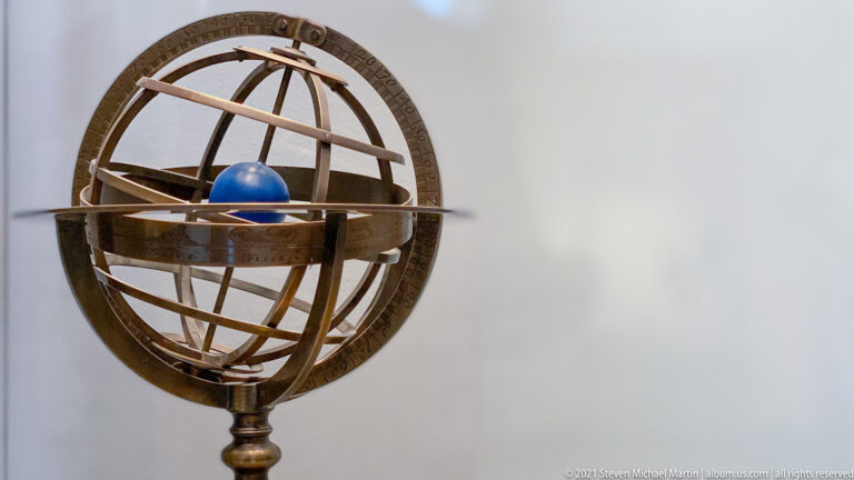 Armillary sphere with intersecting bronze-colored rings surrounding a small blue globe on a stand.