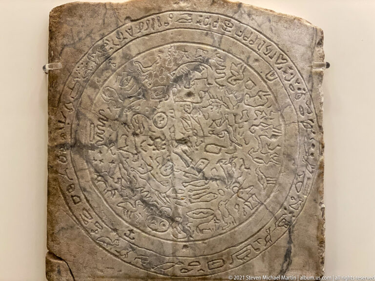 Rectangular stone slab with concentric carved circles, small figures or symbols, and an inscription around the perimeter.