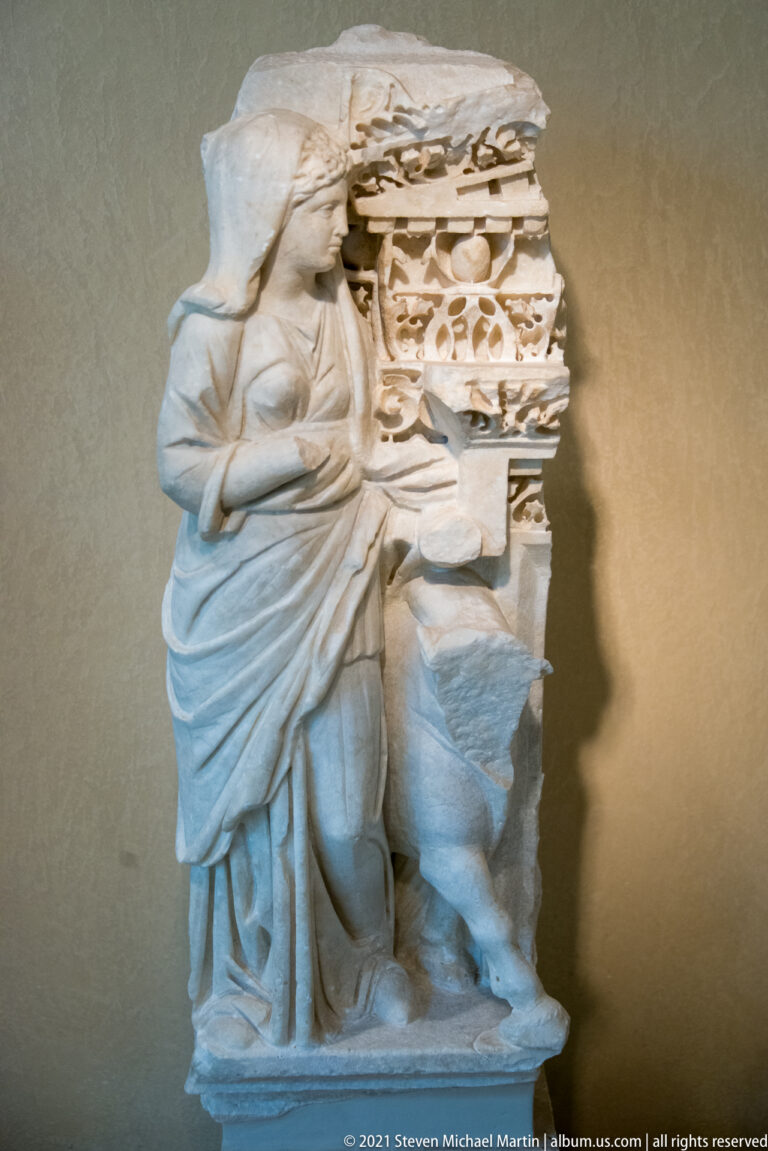Fragmentary marble sculpture of a draped figure beside densely carved architectural ornament.