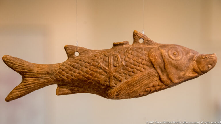 Fourth- to fifth-century clay hanging lamp shaped as a fish, with modeled scales, suspension holes, and Christian symbols.