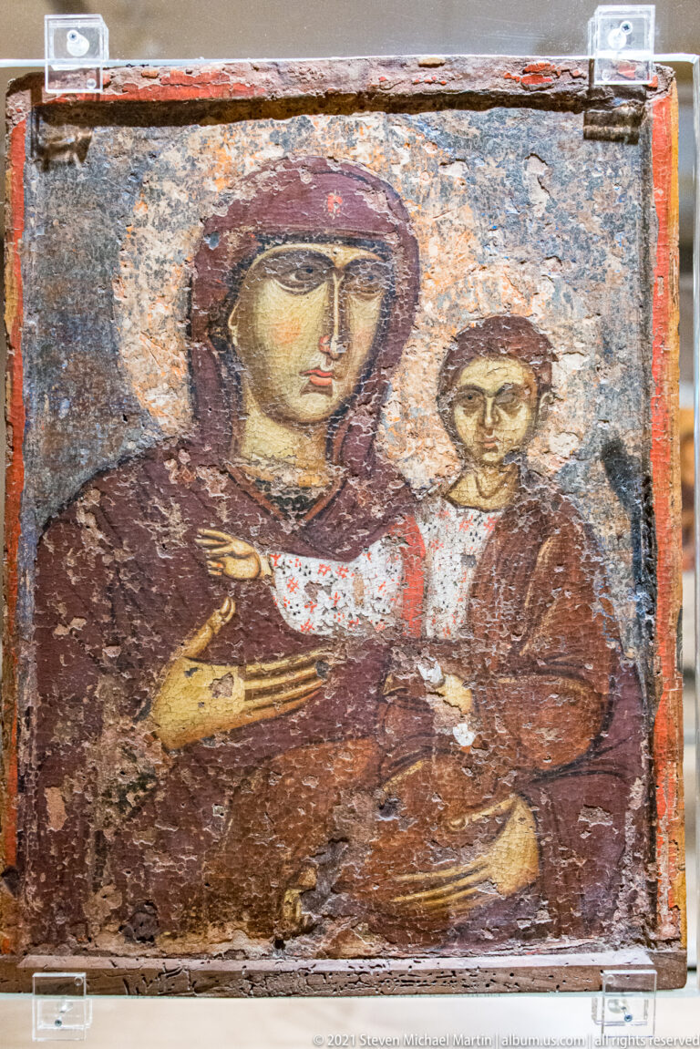 Weathered icon of the Virgin holding the Christ Child, with worn dark background and red-brown garments.