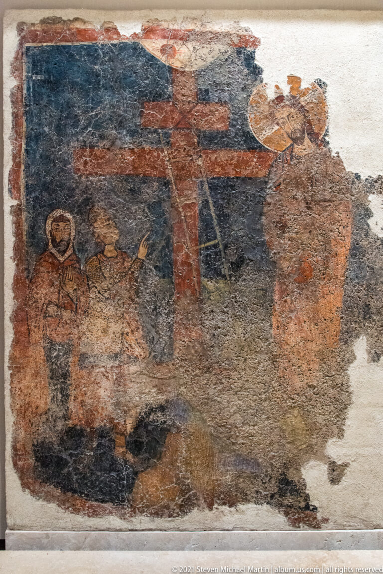 Fragmentary fresco on worn plaster with a small haloed figure and partial larger standing figures.