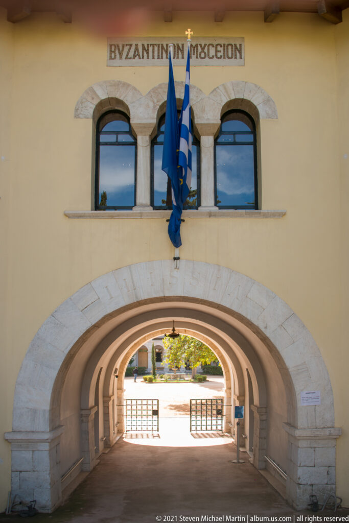 Stone-trimmed arched passage through the museum building, with paired windows and flags above.
