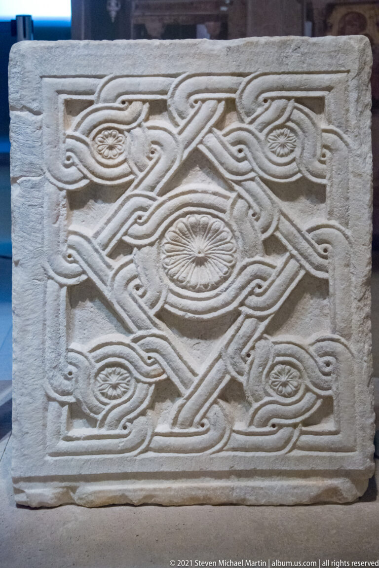 Rectangular stone relief carved with symmetrical interlace, circular rosettes, and leaf-like motifs inside a raised border.