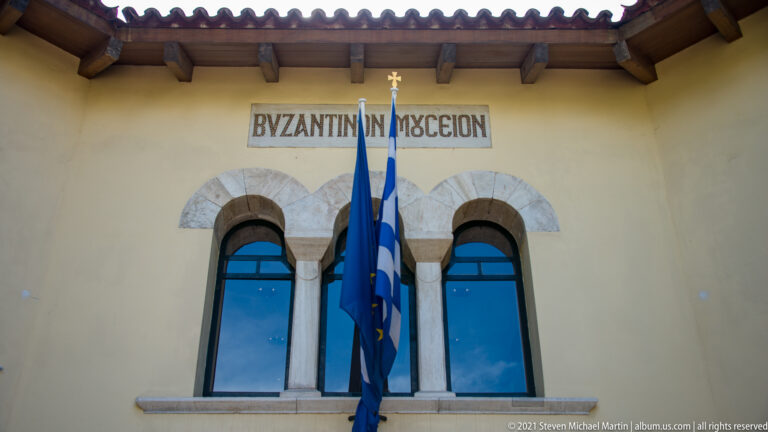 Paired arched windows with Greek museum lettering and two flags hanging between them.