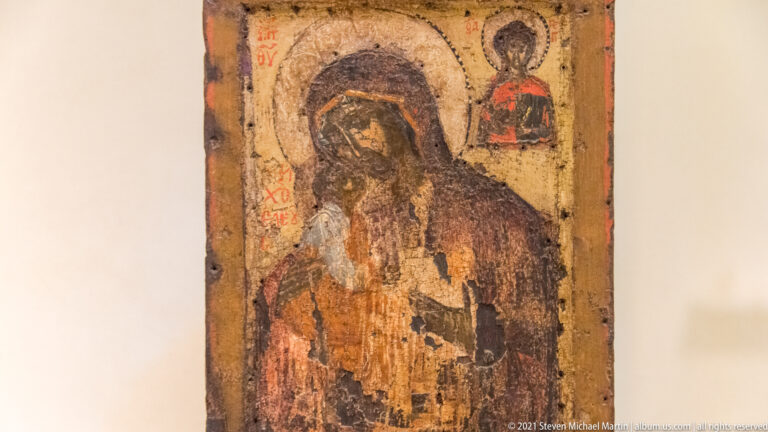 Heavily worn icon of the Virgin and Child with a smaller standing haloed figure in the upper right corner.