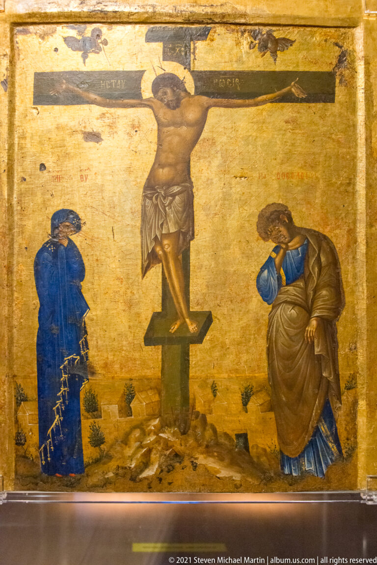 Crucifixion icon with Christ on the cross between two mourners, a skull below, and an inscription above.