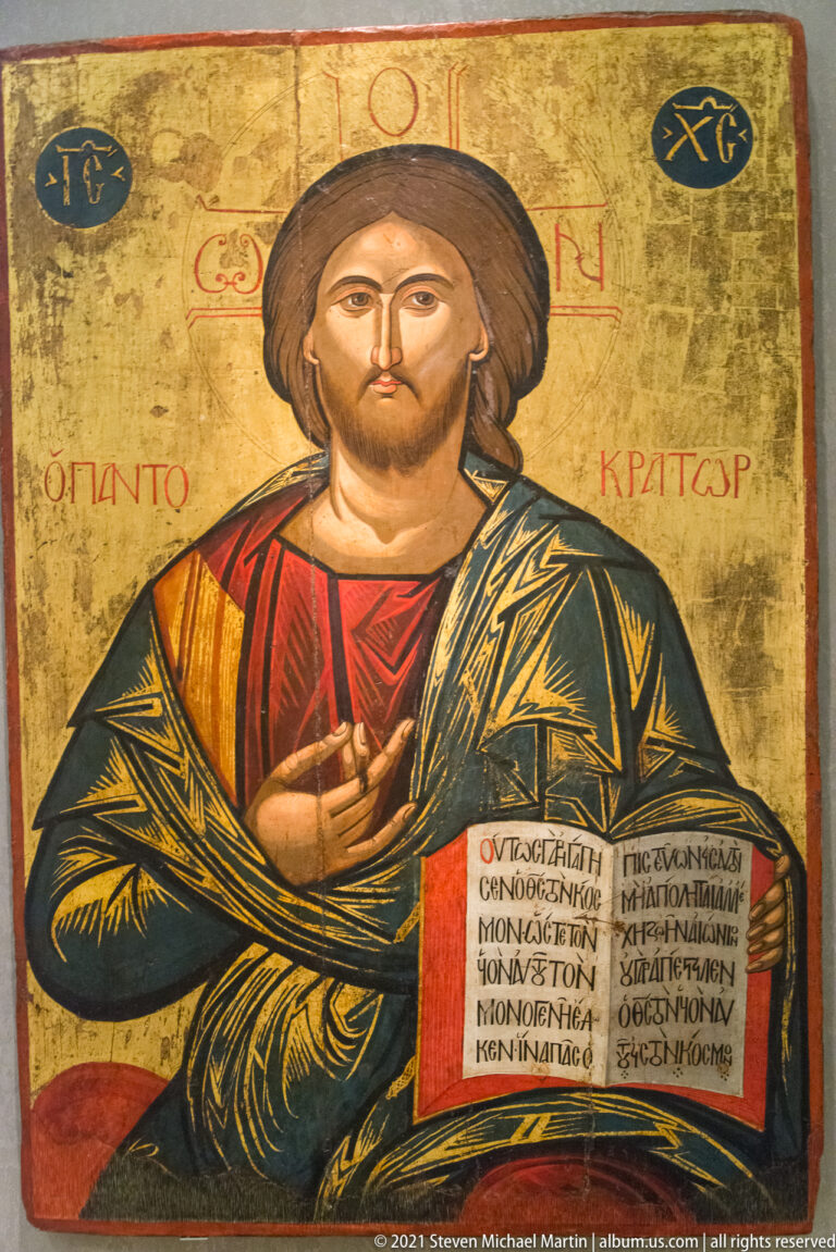 Half-length Christ Pantocrator blessing and holding an open Greek-inscribed Gospel book against a gold ground.
