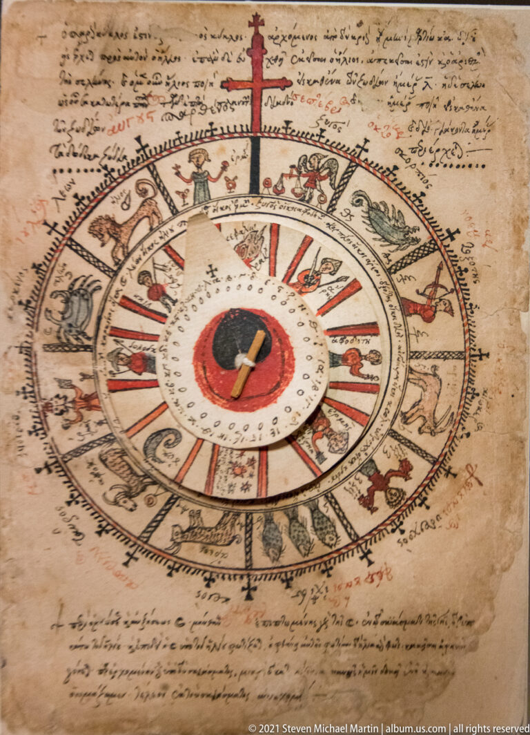 Manuscript page with concentric circular diagram, zodiac-like figures, radial divisions, central disk, and handwritten Greek notes around it.