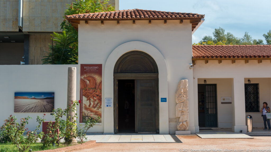 Round-arched museum doorway flanked by carved stone fragments, display panels, and a vertical banner.