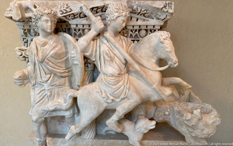 Carved stone relief with a horseman, standing figure, horse, and a smaller figure beneath.