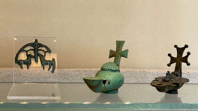 Three small metal Christian objects, including openwork and patinated crosses, displayed together in a museum case.