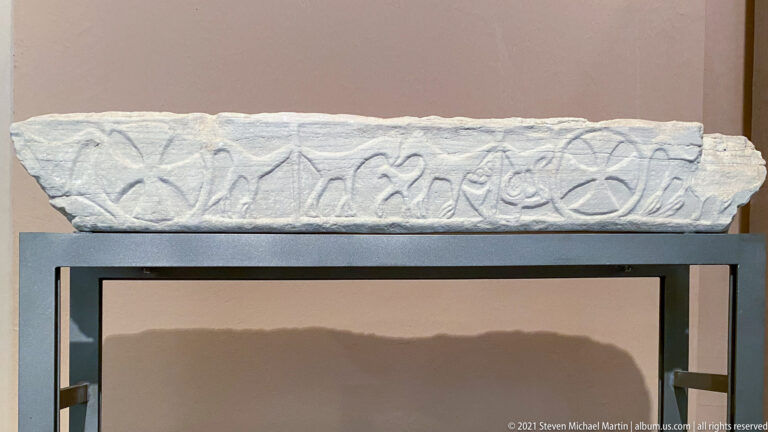 Long white marble fragment on a stand, carved with a continuous band of linked loops and heart-shaped motifs.