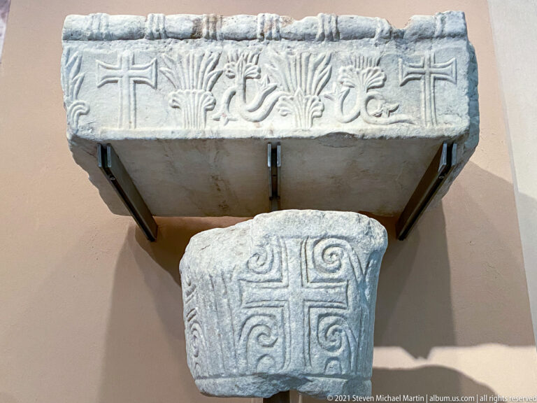 Two marble architectural fragments, one carved with birds and vegetation and the other with a geometric cross pattern.