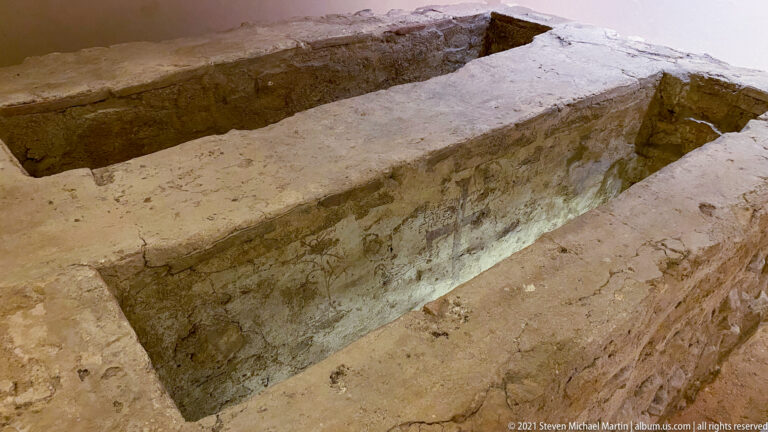 Excavated rectangular masonry channels or foundations preserved below the floor inside the museum.