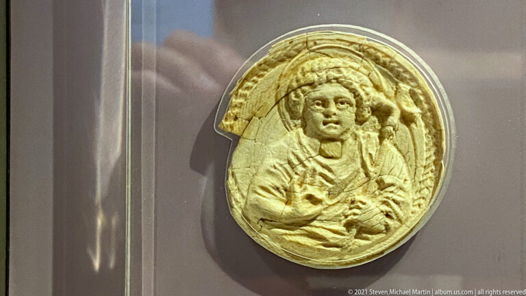 Small pale oval devotional relief with a frontal haloed figure raising one hand.
