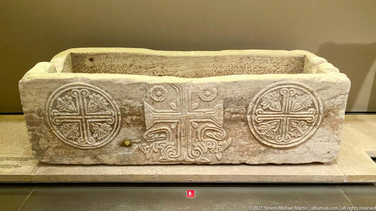 Rectangular marble chest with two circular cross medallions and an ornate central cross carved on the front.