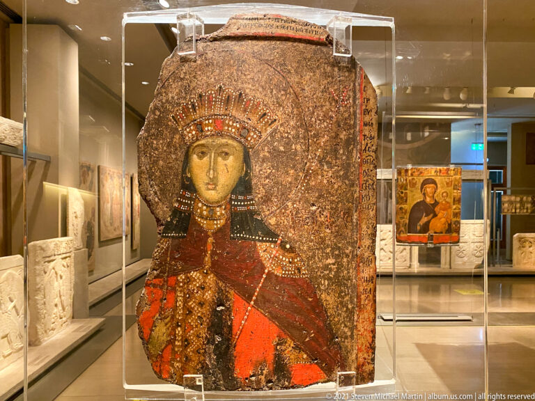 Large worn icon of a frontal female holy figure in jeweled red robes and an elaborate headdress.