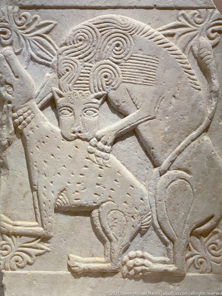 Pale stone relief carved with two overlapping animals, including a large quadruped above a smaller animal.
