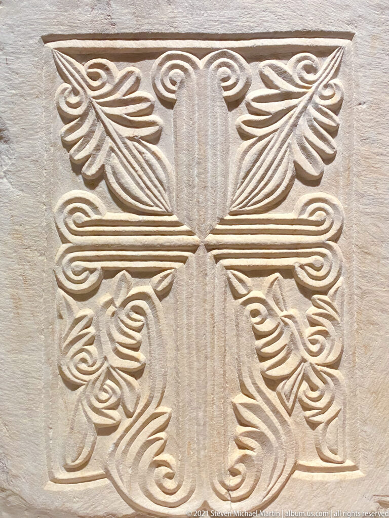 Close-up of a marble relief cross with grooved arms and symmetrical leaf-like carved terminals.