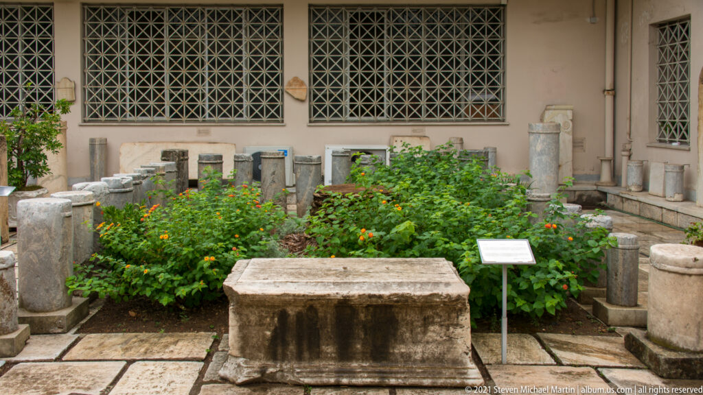 Museum courtyard garden surrounded by low stone blocks, stelae, and cylindrical inscribed monuments.