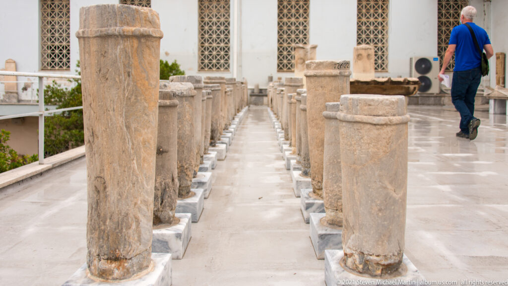 Long aisle between parallel rows of upright stone stelae and cylindrical monuments on individual bases.