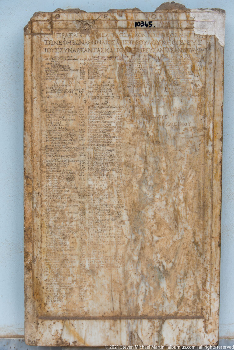 Large weathered rectangular marble slab with dense lines of Greek inscription inside a ruled border.
