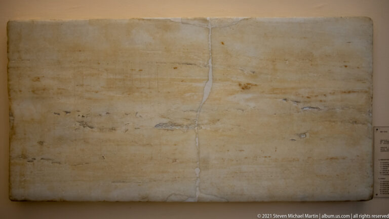 Broad pale marble slab with very faint horizontal inscription and a vertical repaired seam near the center.