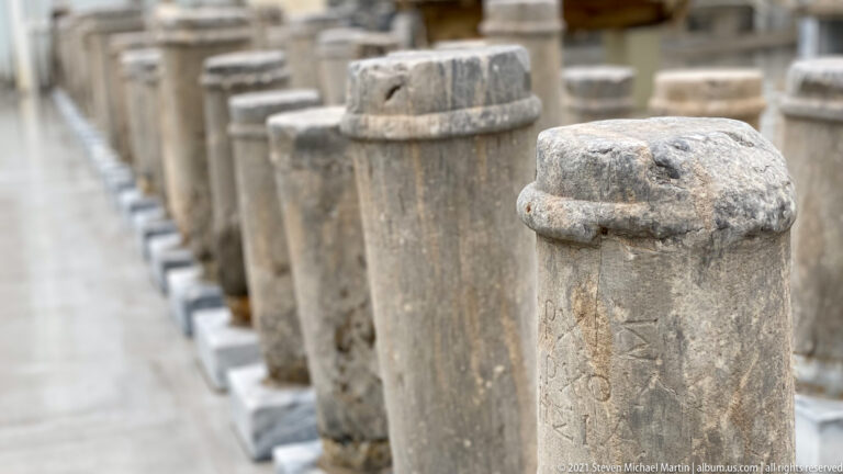 Close perspective along a row of weathered upright stone shafts and stelae, with the nearest monument in focus.