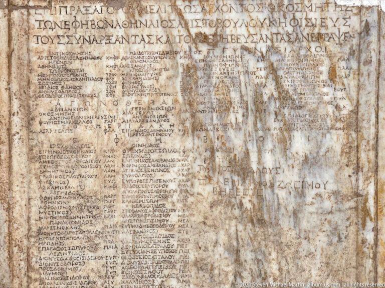 Large weathered marble slab densely covered with Greek text in multiple sections and varying letter sizes.