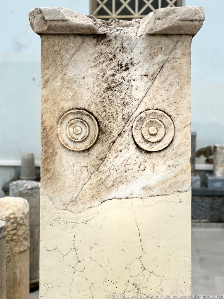 Weathered marble stele with two carved concentric circular motifs and a diagonal crack across its upper face.