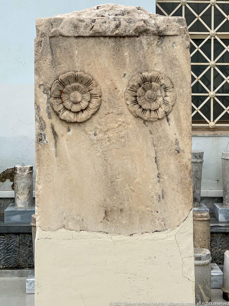Marble stele fragment with two carved multi-petaled rosettes beneath a projecting top edge.