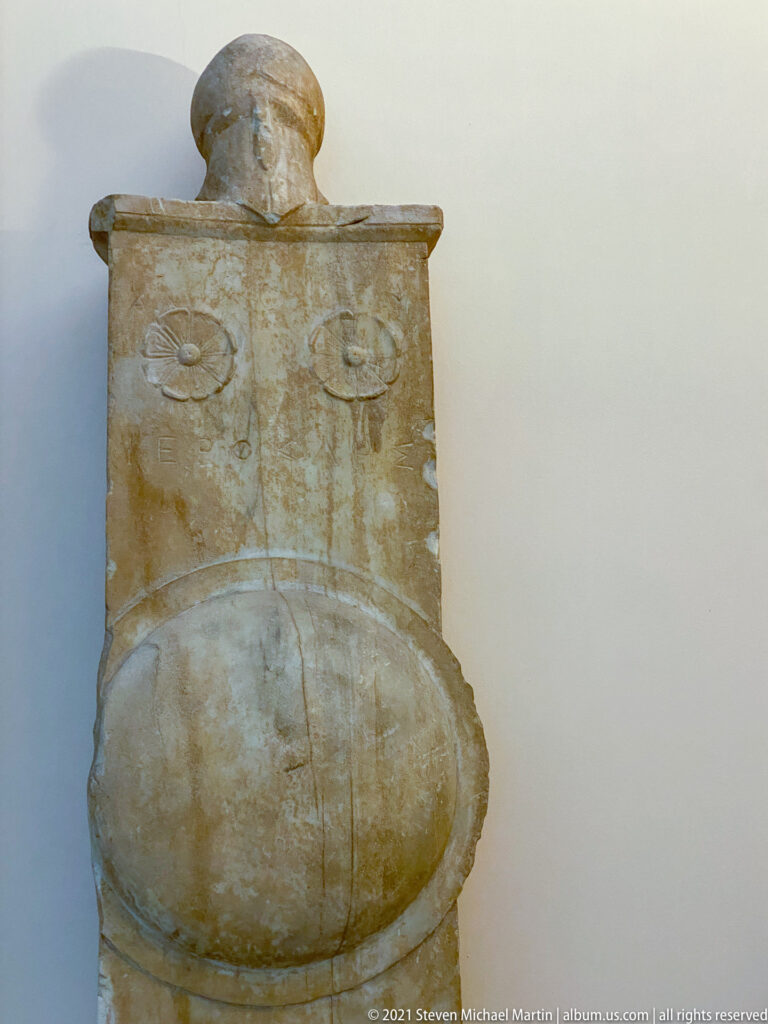 Bulbous marble funerary monument with squared upper section, projecting rim, and two shallow circular ornaments.