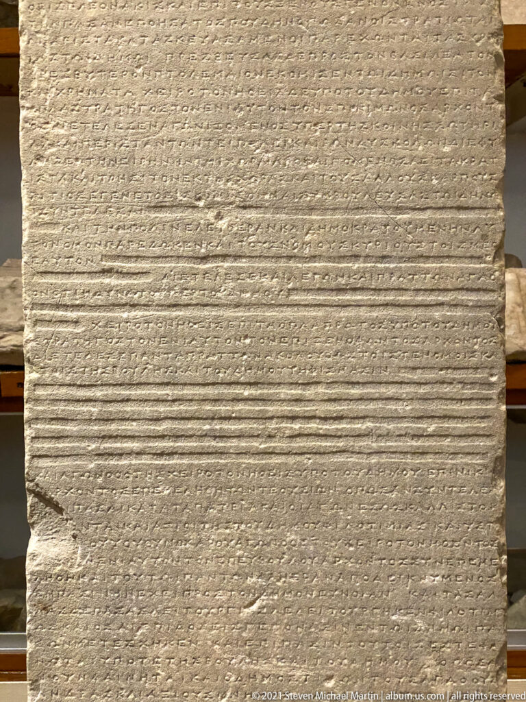 Large marble slab densely covered with horizontal lines of Greek inscription and several shallow bands across the center.