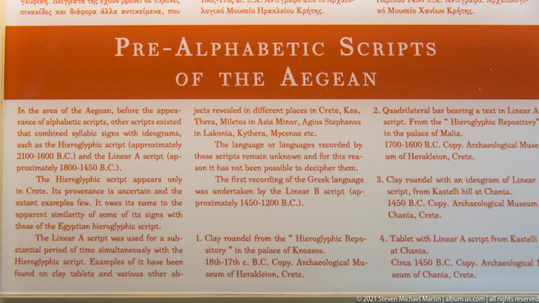 Orange museum panel headed “Pre-Alphabetic Scripts of the Aegean,” with explanatory text and numbered examples.
