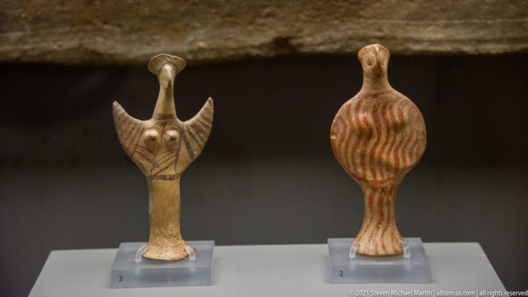 Two small painted ceramic female figurines, one with raised angular arms and one with a rounded striped body.