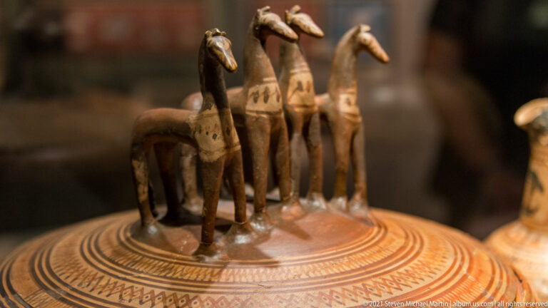 Close-up of several small modeled horses standing on a painted ceramic vessel lid above concentric geometric bands.