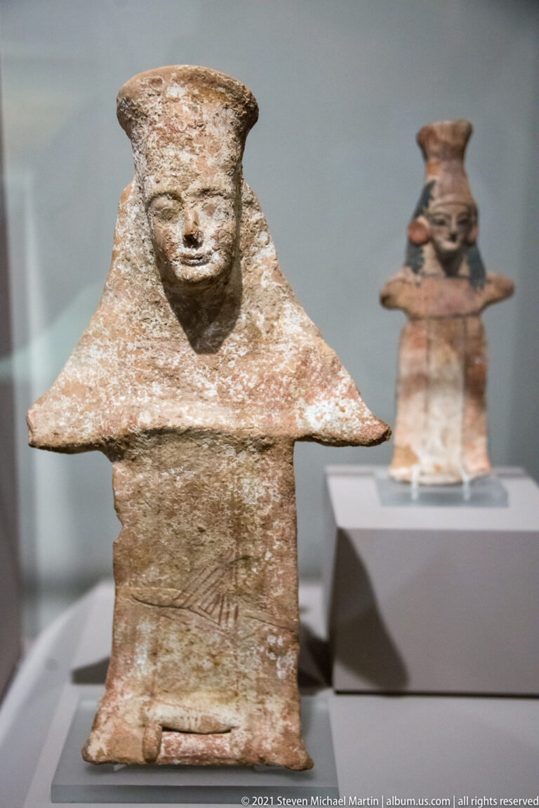 Flat terracotta female figurine with modeled head, broad triangular shoulders, rectangular body, and faint linear decoration.