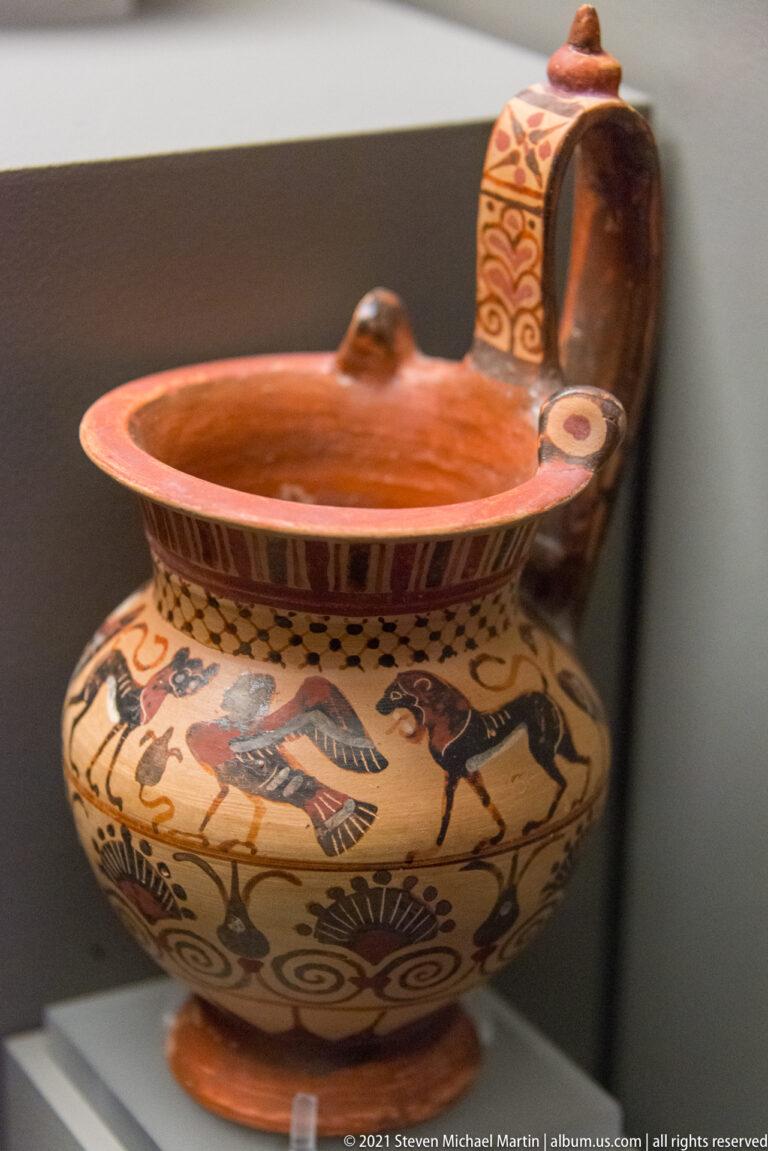 Open painted ceramic vessel with rounded body, animal-and-human frieze, and a tall decorated attachment behind the rim.
