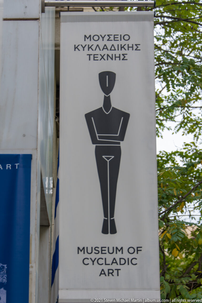 Vertical Museum of Cycladic Art banner with Greek and English names and a black stylized human-figure logo.