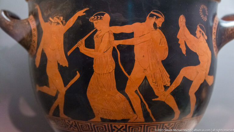 Red-figure pottery detail with several gesturing human figures on a glossy black ground.