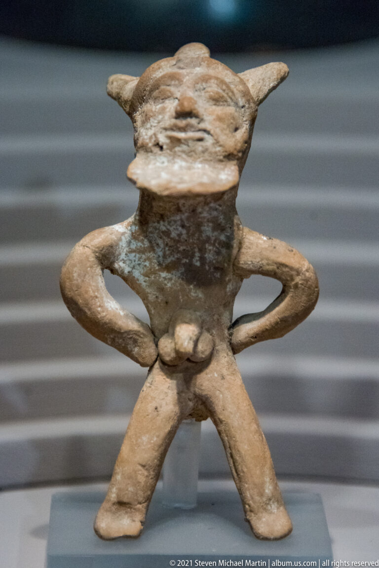 Small terracotta anthropomorphic figure standing with hands on hips and legs apart.