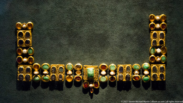 Gold necklace or pectoral with rows of multicolored stones and a large green central setting.