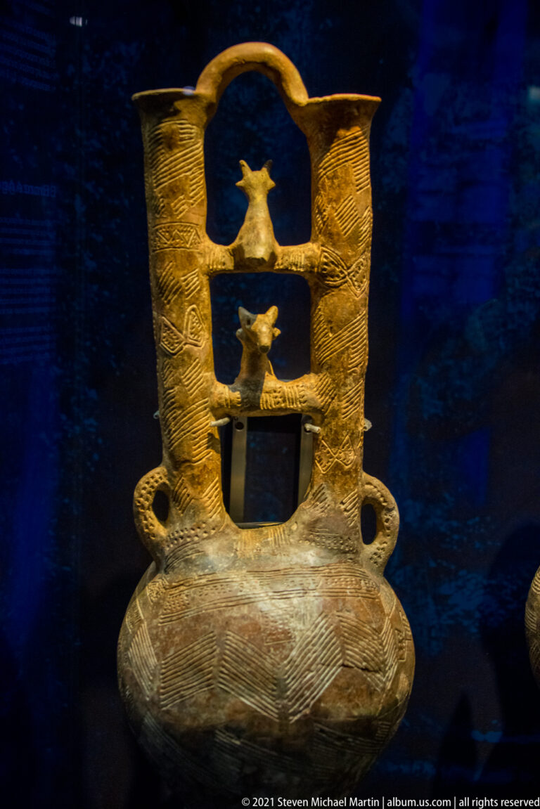 Ceramic vessel with openwork neck containing small modeled animals and geometric incised decoration.