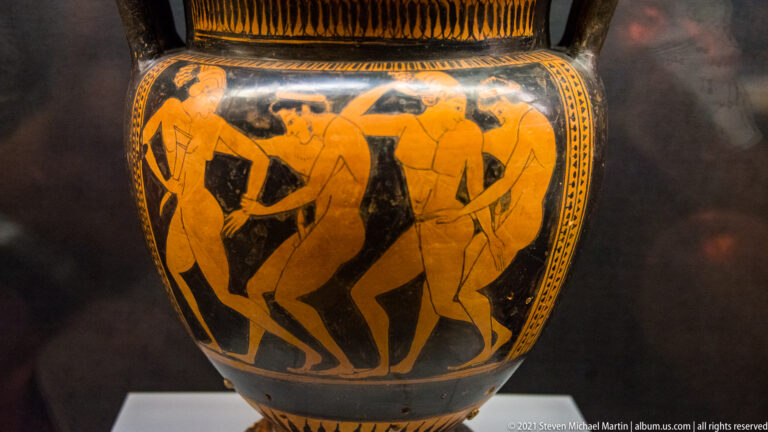 Attic black-figure lekythos with five male revelers dancing in a Dionysian komos around a central draped figure.