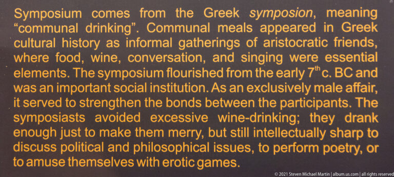 Orange museum text panel explaining the social customs of the ancient Greek symposium.