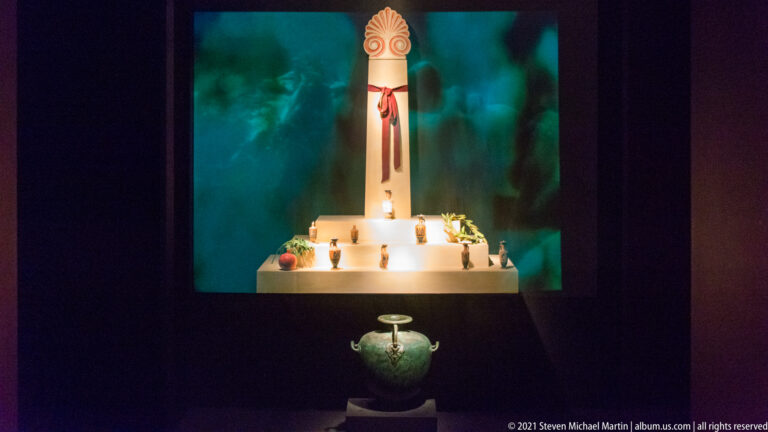Dark museum installation with a green vessel below a tall illuminated architectural display.